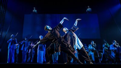 Twee dansers in dezelfde houding voor op het toneel met zangers en dansers daaromheen