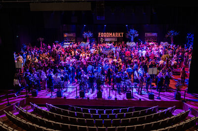 Een druk bezochte evenement met veel mensen, gekleed in feestelijke kleding, onder kleurrijke podiumverlichting.