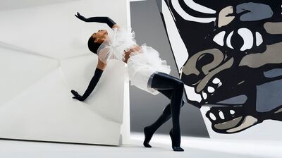 Dansperformer in witte outfit met tule, poseert tegen abstracte achtergrond met zwart-wit kunstwerk.