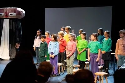 Een groep kinderen in kleurrijke kleding staat op een podium naast een grote, abstracte pop tijdens een voorstelling.