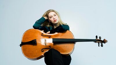 Celliste met haar haar cello horizontaal op schoot waar ze op leunt