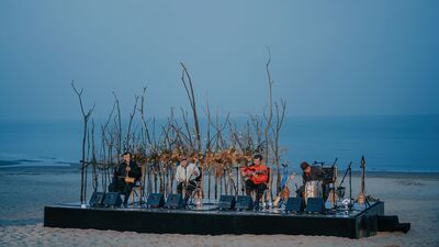 Band op een podium op het strand, omringd met hoge takken