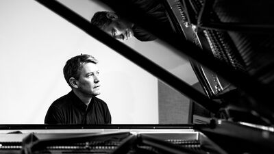 Pianist in zwart wit achter de piano met weerspiegeling in klep van de vleugel
