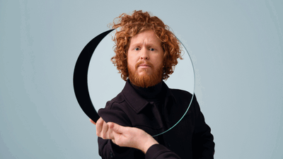 Kasper van der Laan tegen een lichtblauwe achtergrond, met ronde spiegel in zij hand