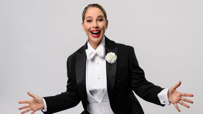 Een vrouw lachend met haar armen breed in een mannelijk pak met corsage