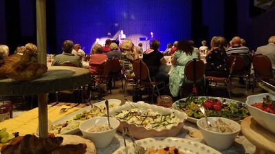 Een dinersetting met diverse gerechten op een tafel, met mensen die naar een opera optreden op het podium kijken.