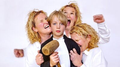 Een jongen staat in het midden omringd door drie vrouwen met krullend haar, die verschillende emoties uitdrukken.