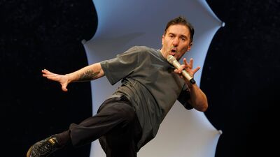 Cabaretier met een microfoon in zijn hand en soort karatehouding met een trap