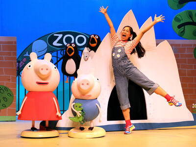 Kind in een overall poseert vrolijk naast Peppa Pig en haar vrienden voor een kleurrijke zoo-decor.