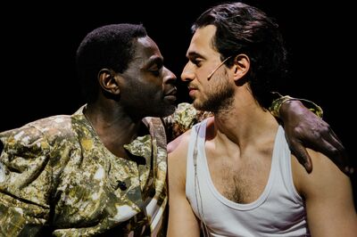 Twee acteurs staan dicht bij elkaar, met intense blikken, een dramatische scène in een voorstelling.