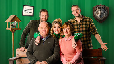 Groep van vijf mensen poseert samen op een bank, met een groene achtergrond en enkele decoratieve elementen.